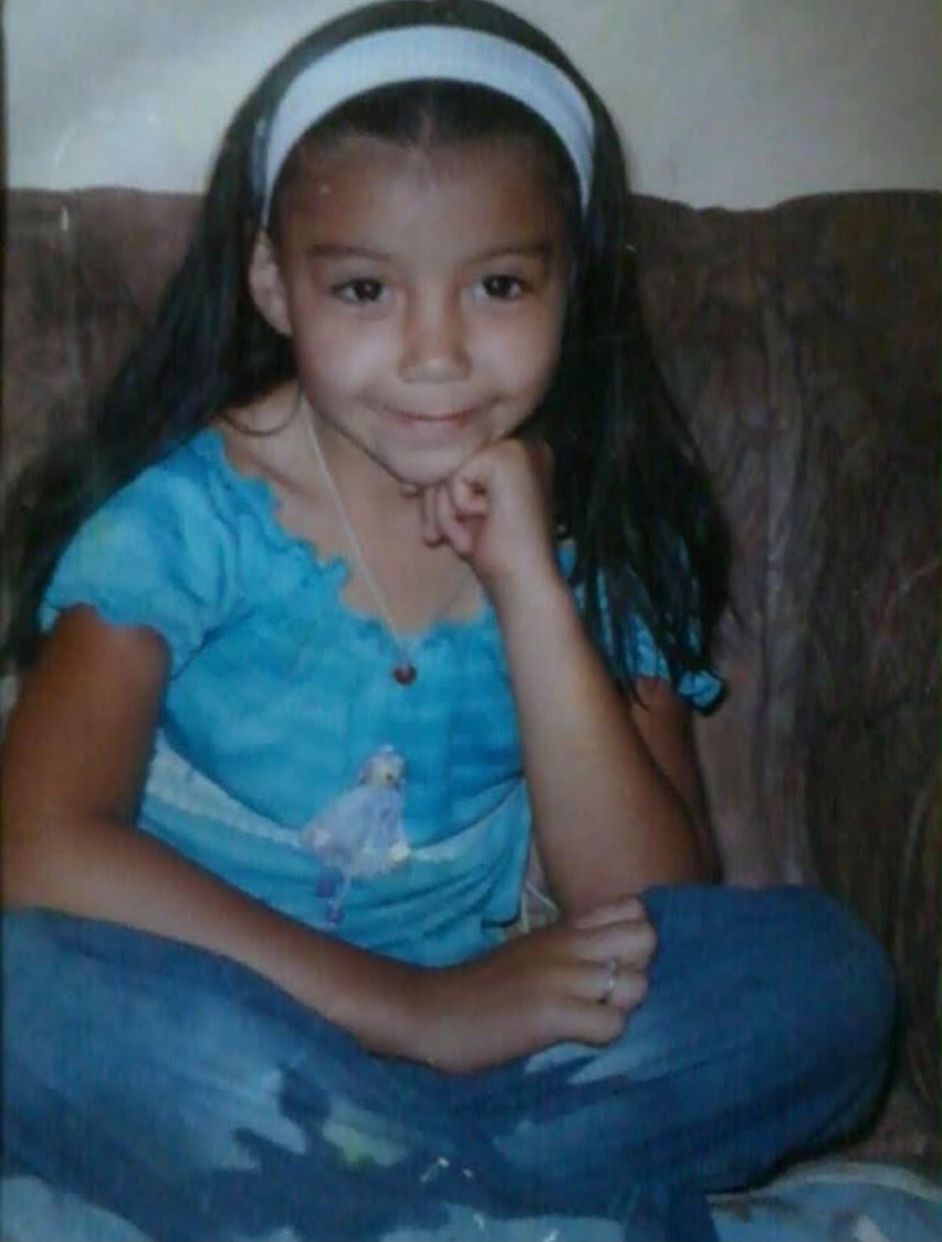 Juliana de niña en casa, sentada con las piernas cruzadas en el sofá familiar
