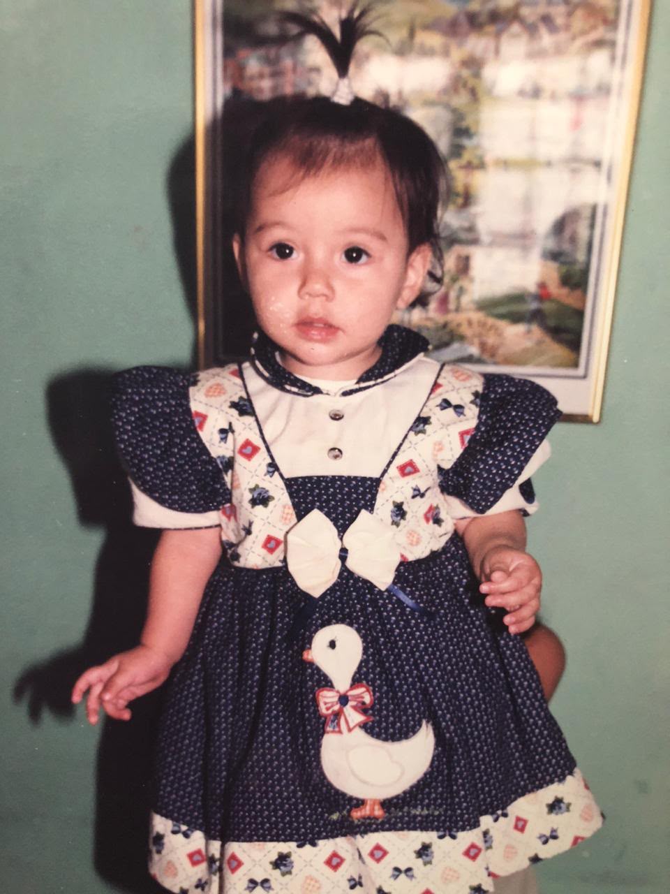 Juliana de pequeña en Colombia, con un vestido azul marino con un pato